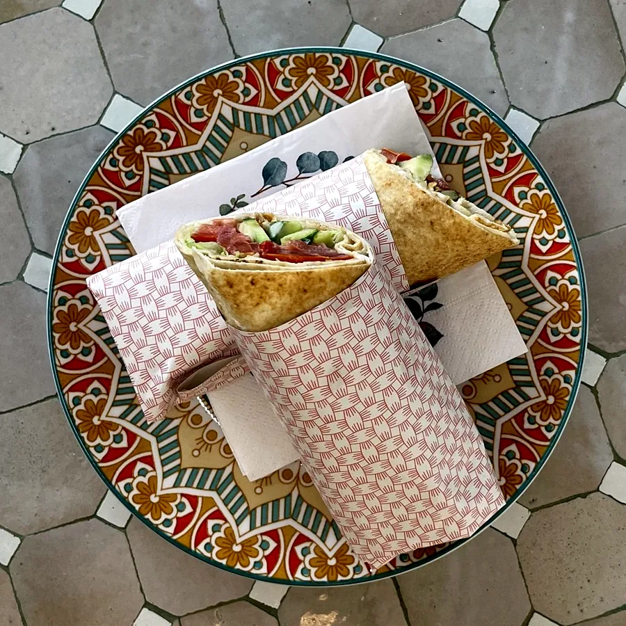 Aufgeschnittener Wrap in To-Go-Papier auf einem bunt gemusterten Teller
